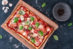 A top view of a rectangular pizza with tomatoes and basil