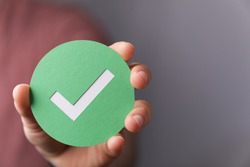 A hand holding a green paper with the checkmark sign on it