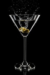 A vertical shot of martini glass with olive and splashes on black background