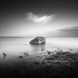 A monochrome shot of an old abandoned shipwreck near the seashore on a gloomy day