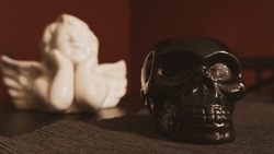 A selective focus shot of a black skull sculpture with a blurred white angel background