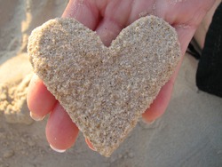 A hand holding a heart made of sand