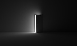 A grayscale shot of an open door letting light into a dark room
