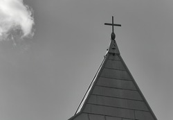 A grayscale shot of a church steeple with a cross against a cloudy sky