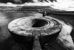 A greyscale shot of a plughole in a lake