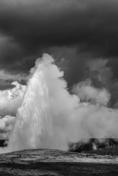 A greyscale interesting shot of a natural fountain on the background of dramatic clouds 