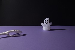 A ghost decoration for Helloween and hand bones on purple black background with copy space