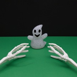 A ghost from Halloween and the bones of the hands that want to catch her on a green-black background