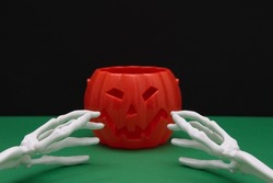 A pumpkin from Halloween and the bones of the hands that want to catch her on a green-black background