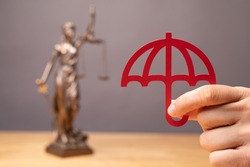 A person's hand holding a red umbrella near the statue of justice