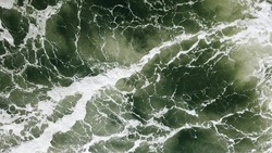 A top view of the white foamy waves and green water texture background