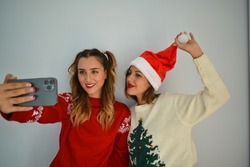 Two young Caucasian females taking selfies wearing Christmas clothes on a white background