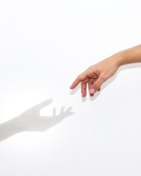 A hand trying to reach the silhouette of a shadow hand on a white background