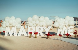 The sign of Marry me in big letters with roses on a beach