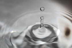 A grayscale closeup of a drop of water hitting a water surface