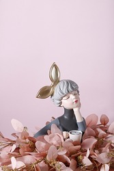 The vertical shot of a fragile porcelain sculpture depicting a girl with a huge golden bow holding a cup of coffee