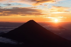 Silhouette of volcano de agua at firey orange sunrise seen from the top of volcano de acatenango, guatemala 