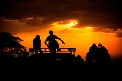 A beautiful silhouette shot of  children dancing on a car roof by sunset golden sky and silhouetted trees