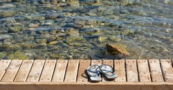 A pair of beach slippers on a boardwalk by the sea