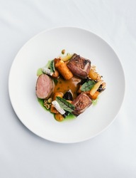 A vertical top shot of a gourmet dish with meat, vegetables, and sauce