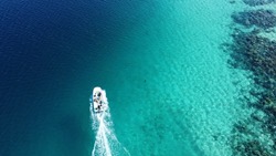 An aerial view of a boat sailing in turquoise water