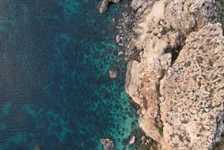 A top view of a blue ocean and a rocky cliff in daylight