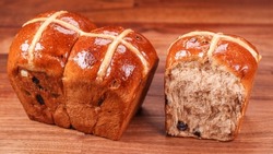 A closeup of fresh cross bun bread with raisins on the wooden surface 