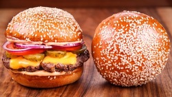 A closeup of a burger with sesame bread on the wooden surface 