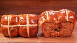 A closeup of fresh cross bun bread with raisins on the wooden surface 