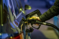 A shallow focus shot of hand of an adult man holding a gasoline pump and filling his car with petrol at gas station at night