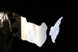 A beautiful view of a silhouetted cave frame on flowing water against a gray sky