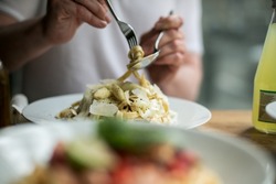 A Food editorial of a restaurant setting with visible hands twirling pasta and plates at the table