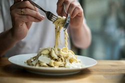 Food editorial of a restaurant setting with visible hands twirling pasta and plates at the table