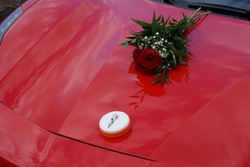 A set of engagement rings and a bouquet of red roses on a red Ferrari