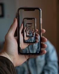 A vertical shot of a person holding a smartphone with many trippy mirroring repetitions of the same image on the screen 