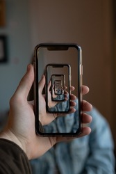 A vertical shot of a person holding a smartphone with many trippy mirroring repetitions of the same image on the screen 