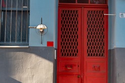 An old red closed wooden door of a building with wrought iron mesh