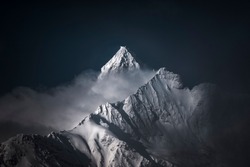 A high-angle shot of snowy mountains covered with clouds during a dark evening