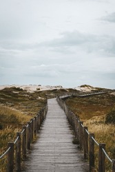 A vertical shot of a wooden pathway in a green coastal field on a cloudy day