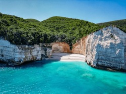 4K Drone shot of a little cove next to Fteri Beach, Kefalonia, Cephalonia, Greece with a lonely figure, surrounded by cliffs and greenery.