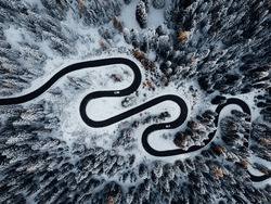 An aerial shot of a winding road cutting through a wintery snowy landscape with evergreen trees lining the route