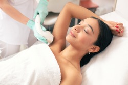 Calm young woman lying with closed eyes and putting on arm up while having laser hair removal procedure on it