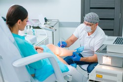 Professional doctor in a medical mask using modern equipment while curing veins on the leg of his patient