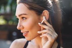 Close up portrait of a lovely young fitness girl listening to music through wireless earphones outdoors