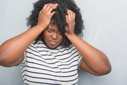 Young african american plus size woman over grey grunge wall suffering from headache desperate and stressed because pain and migraine. Hands on head.
