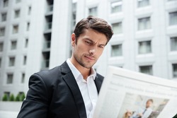 Serious young businessman reading newspaper in the city