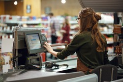 Back view photo of cashier woman on workspace in supermarket shop. Looking aside.