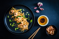 Asian food - noodles with prawns in soy sauce with spinach on black table