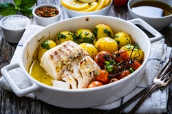 Fish dish - baked cod fillet with potatoes and cherry tomatoes on wooden table 