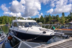 A white luxury yacht is moored at the pier in marina on a summer day. Wooden jetty pier berth. Parking for yachts and boats. Yachting equipment. People lifestyle. The Stockholm archipelago in Sweden.